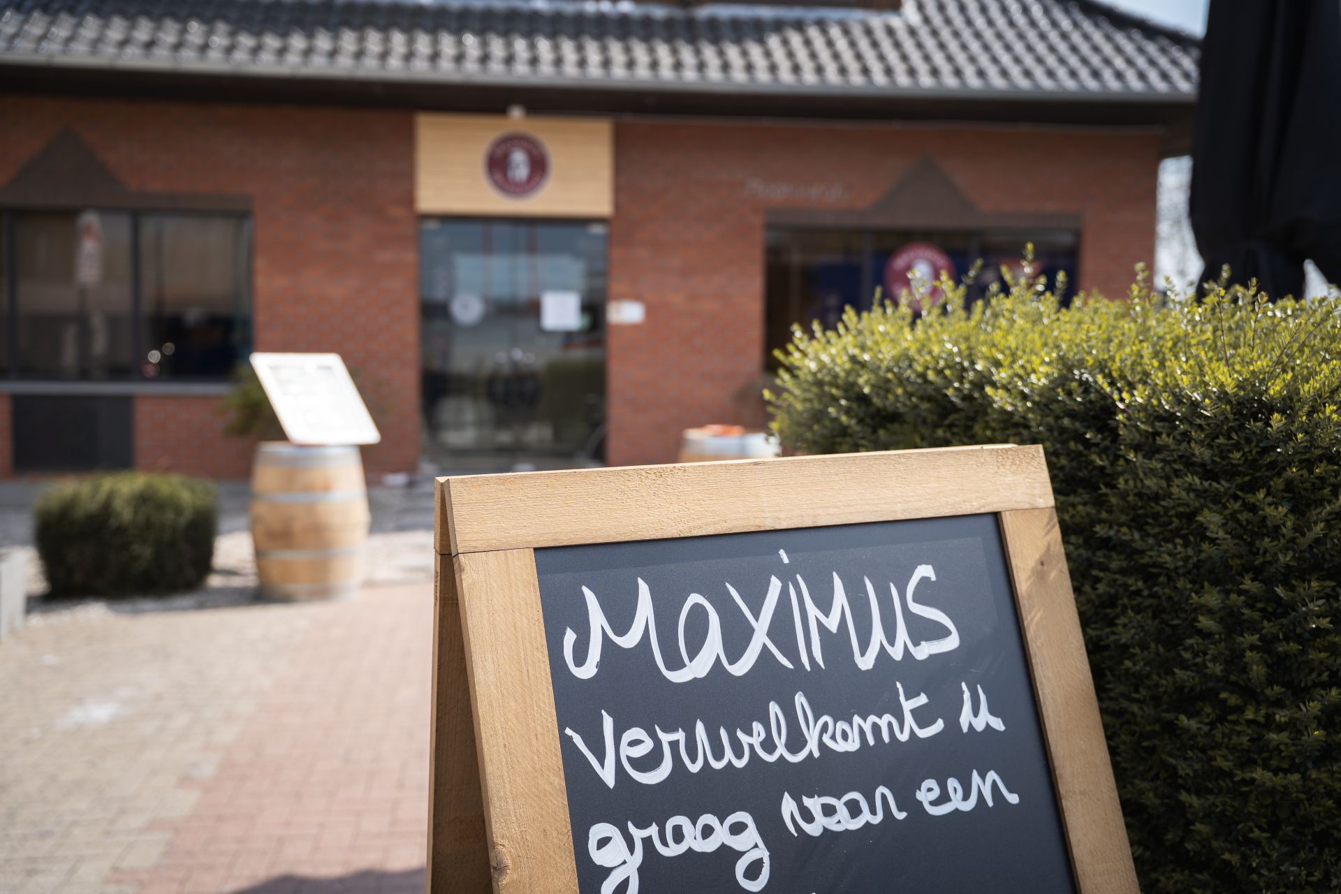 Vue extérieure du l'avant du restaurant Maximus Steakhouse Halle avec vue sur un panneau avec le texte "Maximus verwelkemt u graag vaar een" écrit à la craie.