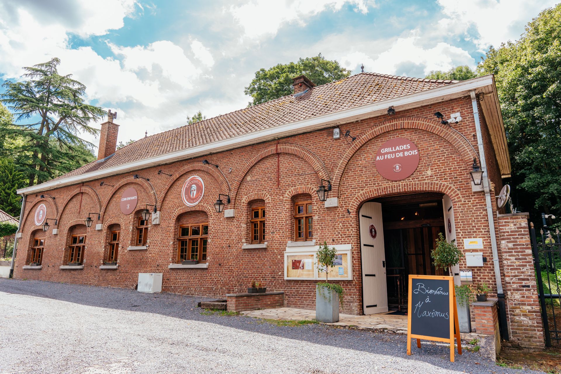 Vue sur l'extérieur du restaurant de Maximus Steakhouse Mons. Le bâtiment rustique a des murs avec briques classiques et la porte est grande ouverte.