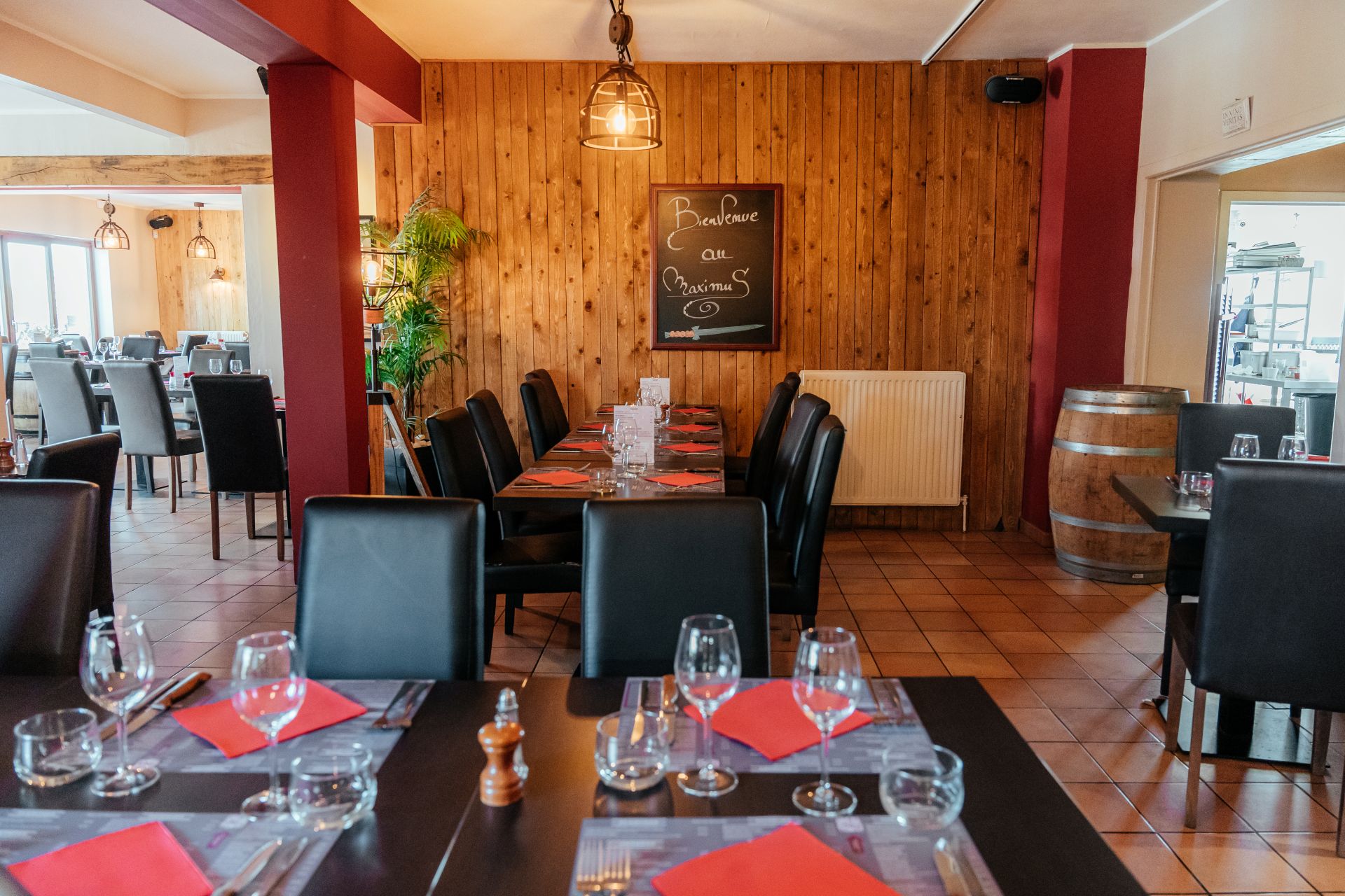 Vue de l'intérieur du restaurant de Maximus Steakhouse Nivelles. Tables apprêtées et chaises. Au fond de la pièces, des lattes en bois donnant un air chaleureux. Sur ces lattes en bois, un panneau avec écrit à la craie "Bienvenue au Maximus".