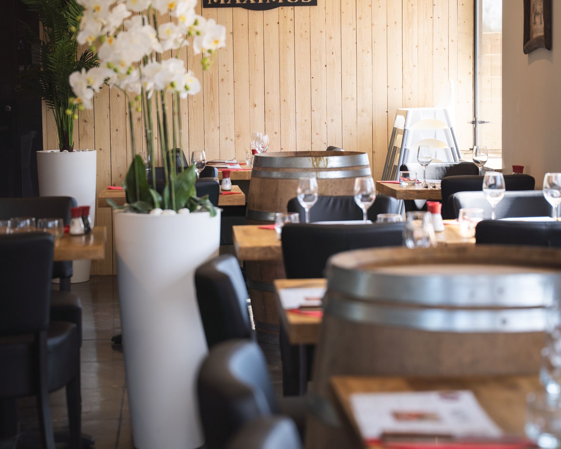 Vue de l'intérieur du restaurant de Maximus Steakhouse Halle. Tables apprêtées et chaises, avec au fond des lattes de bois donnant un air chaleureux à la pièce.